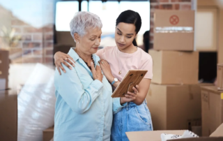 Older woman and young woman look at framed photo in room surrounded by boxes